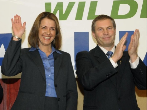 Danielle Smith waves alongside Paul Hinman, who applauds, in front of a Wildrose Alliance banner in October 2009